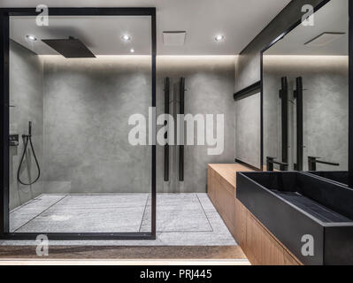 Badezimmer in einem modernen Stil mit grau gefliesten Wänden. Es gibt eine Dusche mit Glastrennwand Stand aus Holz mit einem schwarzen Waschbecken und Wasserhahn, einen großen Spiegel, Stockfoto