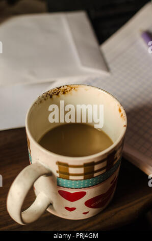 Weiße Tasse Kaffee auf einem hölzernen Schreibtisch, im Hintergrund ein Notebook und die Tastatur eines Laptops. Start Woche Konzept, Arbeit zu Hause Stockfoto