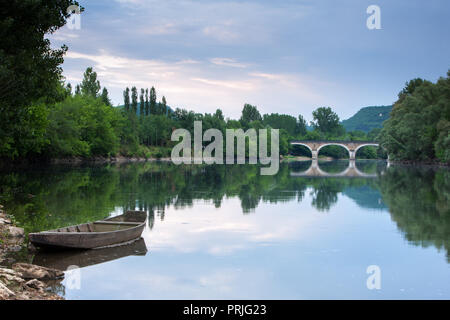 Fluss Dordogne bei Sonnenaufgang mit einem traditionellen hölzernen River Boat und gewölbte Brücke in der Ferne Stockfoto