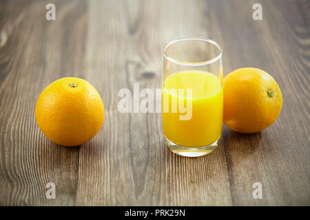 Zwei Orangen und ein Glas Orangensaft auf der Oberfläche des Holzes.