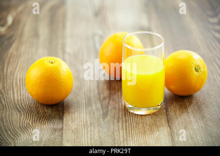 Drei Orangen und ein Glas Orangensaft auf der Oberfläche des Holzes. Stockfoto