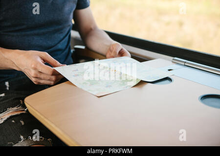 Ein Tourist sitzt am Fenster in einem Zug oder S-Bahn und wirft einen Blick auf eine Karte. Stockfoto