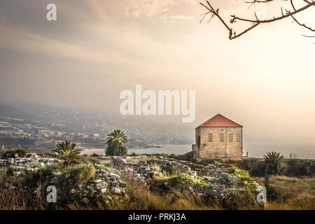 Fantastische Ausblicke auf die Landschaft von Byblos, traditionellen Haus, Felsen, Palmen, Berge im Hintergrund. Haze warmes Licht im Libanon Stockfoto