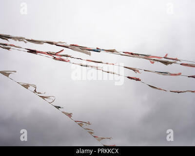 Alte Bunting, Fahnen, Zerlumpte und zerrissen, zerfetzt durch den Wind gegen den grauen Himmel. In den Wind, schlechtes Wetter. Stockfoto