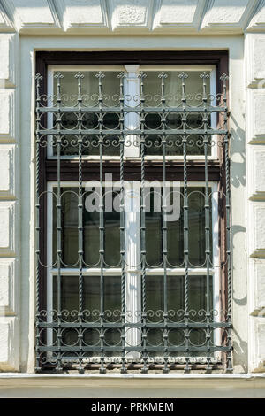 Ein Fenster mit einem Gitter aus Metall und einem hölzernen Fensterrahmens mit einem Gesims gegen eine weiße Wand. Stockfoto