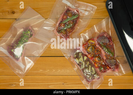 Plastiktaschen mit kleinen Stücken Fleisch neben Schwarz vacuum Sealer über holztisch Hintergrund Stockfoto