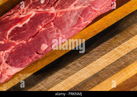 Auf Fettsäuren rot ungekocht Steak sitzen auf zerkratzte Holz Schneidebrett mit diagonalen Streifenmuster schließen Stockfoto