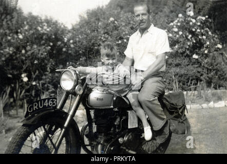 Vater & Sohn für ein Foto auf einem vintage BSA Motorrad im Garten hinter dem Haus in den 50er Jahren darstellen Stockfoto