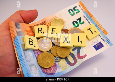 Hand mit Euro-bargeld und Brexit Schriftzug in Scrabble Fliesen auf weißem Hintergrund. Europäische Union Volksabstimmung zu verlassen, Politik Stockfoto