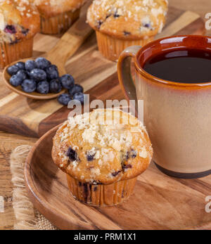 Blueberry Muffin und Tasse Kaffee auf einer Holzplatte mit Beeren und Muffins im Hintergrund Stockfoto