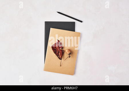 Herbst Konzept des Büros. Ansicht von oben in Braun und Schwarz Notebook mit Blatt, Eichel und schwarzen Stift auf Rose und weißen Hintergrund. Flach mit kopieren Stockfoto