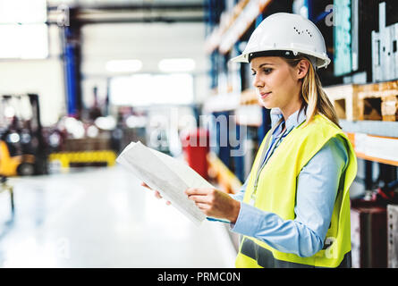 Ein Porträt einer Frau Ingenieur in einer Fabrik holding Schreibarbeit. Stockfoto