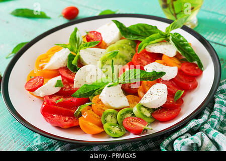 Mozzarella, Tomaten und Basilikum kraut Blätter in der Platte auf die weiße Holztisch. Caprese Salat. Italienisches Essen. Stockfoto