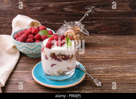 2-in-1-Joghurt mit Müsli und Himbeeren. In einem Glas, mit Minze dekoriert. Auf dunklen rustikalen Holztisch Hintergrund. Gesunde Ernährung Konzept. Stockfoto