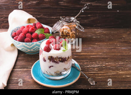 2-in-1-Joghurt mit Müsli und Himbeeren. In einem Glas, mit Minze dekoriert. Auf dunklen rustikalen Holztisch Hintergrund. Gesunde Ernährung Konzept. Stockfoto