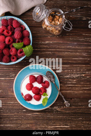 2-in-1-Joghurt mit Müsli und Himbeeren. In einem Glas, mit Minze dekoriert. Auf dunklen rustikalen Holztisch Hintergrund. Gesunde Ernährung Konzept. Stockfoto
