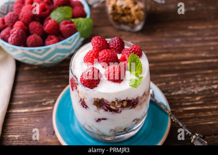 2-in-1-Joghurt mit Müsli und Himbeeren. In einem Glas, mit Minze dekoriert. Auf dunklen rustikalen Holztisch Hintergrund. Gesunde Ernährung Konzept. Stockfoto