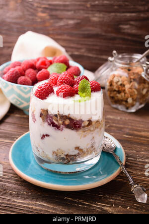 2-in-1-Joghurt mit Müsli und Himbeeren. In einem Glas, mit Minze dekoriert. Auf dunklen rustikalen Holztisch Hintergrund. Gesunde Ernährung Konzept. Stockfoto