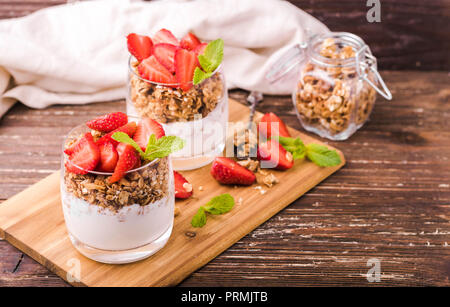 Joghurt Parfait in Gläsern mit Granola, Erdbeeren und Minze. Auf Holzbrett. Gesundes Frühstück Konzept. Rustikalen Holztisch Hintergrund. Stockfoto
