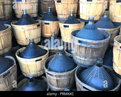 Wein in Flaschen, Glasballons Korbmacherwaren draußen auf der Farm eingeschlossen Stockfoto