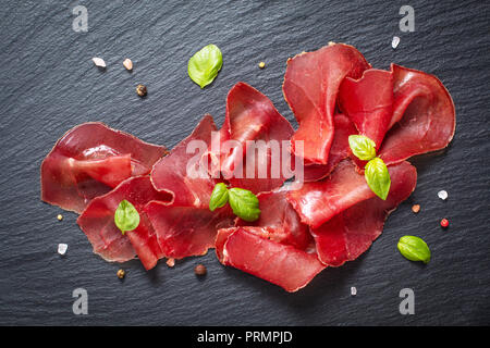 Essen Vorspeise Konzept in Scheiben geschnittene Getrocknete geheilt beefs Bresaola auf schwarzem Schiefer board Stockfoto
