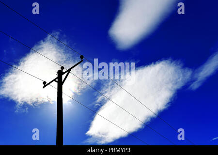 Power Comms Kabel und Pole gegen den tiefblauen Himmel und drei weiße Wolken und rote Aura Stockfoto