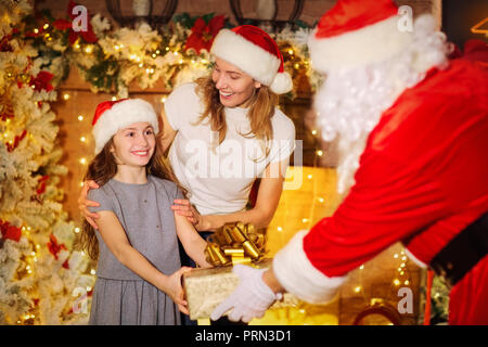 Santa Claus gibt ein Geschenk für ein Mädchen für Weihnachten im Zimmer. Stockfoto