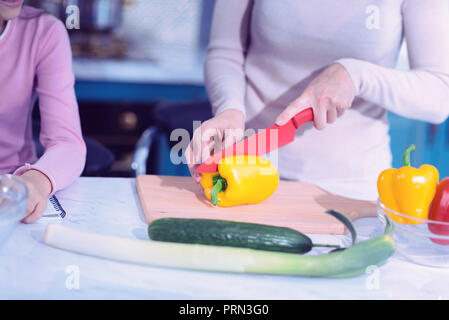 Junge Frau mit einem scharfen Messer vorsichtig Schneiden von Gemüse Stockfoto