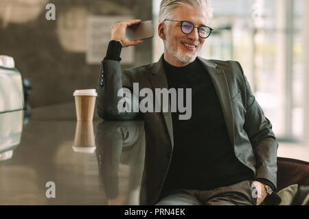 Entspannt älterer Menschen in Gespräch am Handy im Cafe. Reifen Geschäftsmann sitzt locker im Cafe mit Smart Phone. Stockfoto