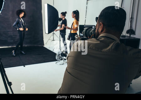 Weibliche Model posiert für Porträts auf schwarzem Hintergrund in einem Studio. Fotograf mit seiner Crew beim Fototermin im Studio. Stockfoto