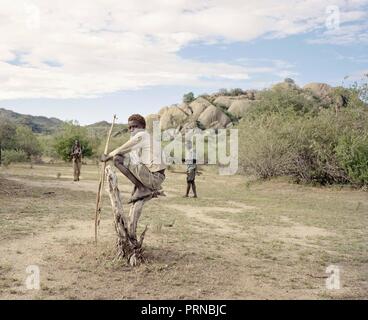 Oktober 3, 2018 - Lake Eyasi, Ngorongoro, Tansania - Osama (15) sitzt auf einem toten Baum. Die hadza sind eine der letzten verbleibenden Gesellschaften, die in der Welt bleiben, dass rein vom Jagen und Sammeln überleben. Sehr wenig wurde in der Art und Weise, wie der Hadza ihr Leben verändert. Aber es wurde immer schwieriger für sie zu verfolgen die Hadza Lebensart geworden. Entweder die Hadza wird einen Weg finden, ihr Land zu sichern - Rechte den Zugang zu sauberem Wasser quellen und wilden Tieren, oder die Hadzabe lifestyle verschwinden werden, wobei die meisten von Ihnen werden nicht zu arm und ungebildet Personen mit Stockfoto