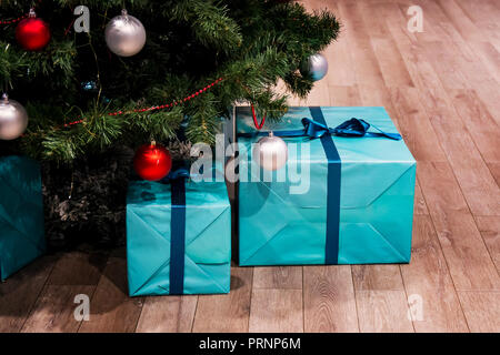 Weihnachten grüner Baum mit Dekorationen und Geschenke unter es in loft Interieur. Große blaue Kästen in einer Geschenkverpackung mit einer Schleife. Real Natural Fichte Stockfoto