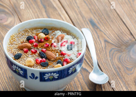 Kleine asure Schüssel leckeres Müsli mit Nüssen und Obst neben kleinen Löffel sitzen auf braunem Holz plank Tabelle Stockfoto