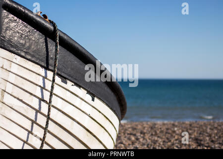 Nahaufnahme von einem Fischerboot am Strand mit Kieselsteinen und Meer im Hintergrund mit einem Seil hängend Stockfoto