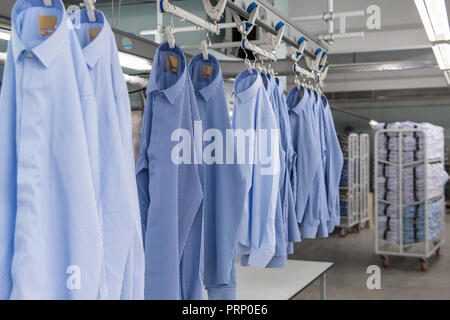 Die neuen Shirts genäht auf Kleiderbügeln hängen in der Textilfabrik workshop Stockfoto