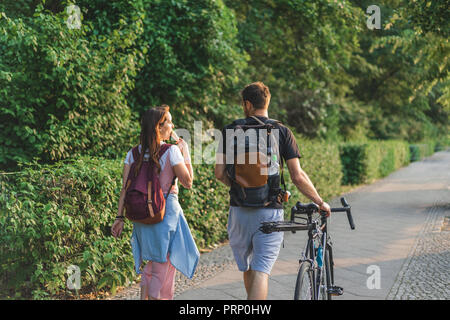 Ansicht der Rückseite Frau Eis essen, während ihr Freund in der Nähe zu Fuß mit dem Fahrrad auf der Straße Stockfoto