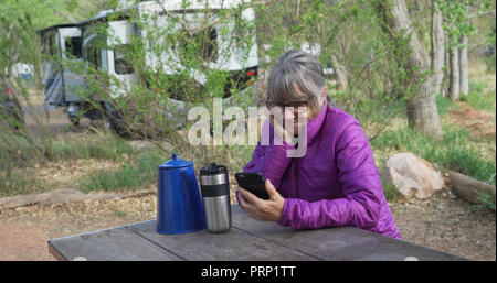 Active Senior Frau auf parkbank Textnachrichten auf Smart Phone in der Natur Stockfoto