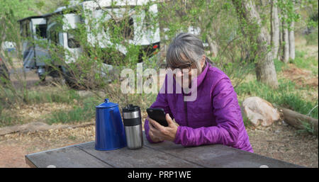 Active Senior Frau auf parkbank Textnachrichten auf Smart Phone in der Natur Stockfoto