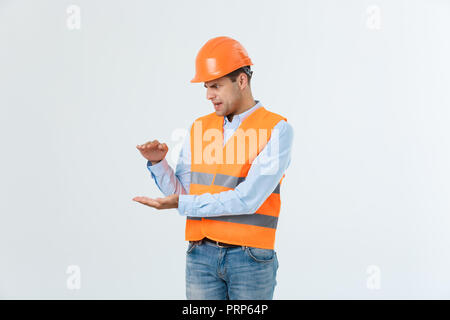 Happy Bart Ingenieur die Hand auf die Seite legen und etwas erklären, Guy tragen caro Shirt und Jeans mit gelber Weste und Helm, orange auf weißem Hintergrund Stockfoto