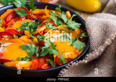 Shakshuka, Spiegelei, Tomaten und Paprika Sauce aus Gusseisen Skillet auf rustikalen Holztisch gekocht Stockfoto