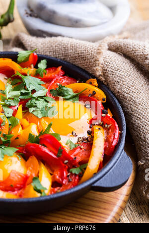 Shakshuka, Spiegelei, Tomaten und Paprika Sauce aus Gusseisen Skillet auf rustikalen Holztisch gekocht Stockfoto