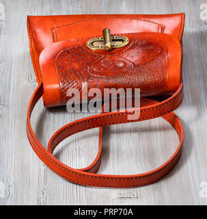 Handgefertigte orangefarbene geprägtem Leder Tasche auf grau Holztisch Stockfoto