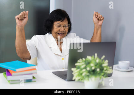 Erfolgreiche ältere Frau Arbeiten am Laptop mit erhobenen Armen Stockfoto