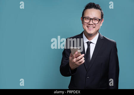 Portrait von Lächeln asiatische Geschäftsmann in Anzug und mit Smartphone. auf hellblauem Hintergrund isoliert. Stockfoto