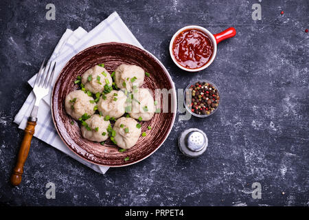 Georgische Knödel Khinkali mit Fleisch, grüne Zwiebeln und Tomatensauce. Auf braun Keramik Platte mit Schale, Sauce, Pfeffer und Salz mischen. Dunkle concr Stockfoto