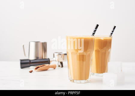 Barista Konzept. Eis Kaffee in ein hohes Glas mit Strohhalm und Milch Krug, portafilter und Holz-/Maßnahme auf weißem Marmor Tabelle über weiß Hinterg Stockfoto