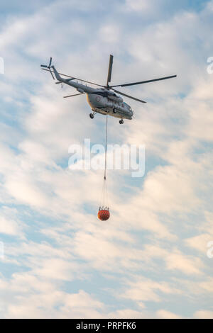 Ein Feuerwehrmann Hubschrauber mit einem vollen Korb von Wasser fliegt gegen einen schönen Himmel Stockfoto