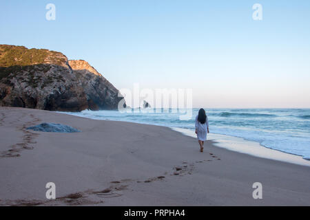 Frau, die zu Fuß auf einem schönen leeren Strand während der Sunrise und trug eine Nacht Kleid Stockfoto