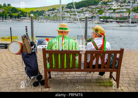 Morris Dancers entspannend auf der Werkbank in Dartmouth, Devon, Großbritannien Stockfoto