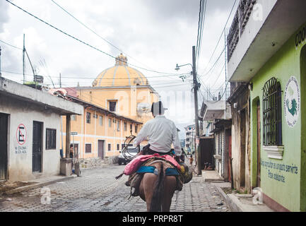 Lokaler Mann reitet Maultier nach unten eine typische Straße in Santa María de Jesús, eine kleine Stadt Antigua in Guatemala Stockfoto